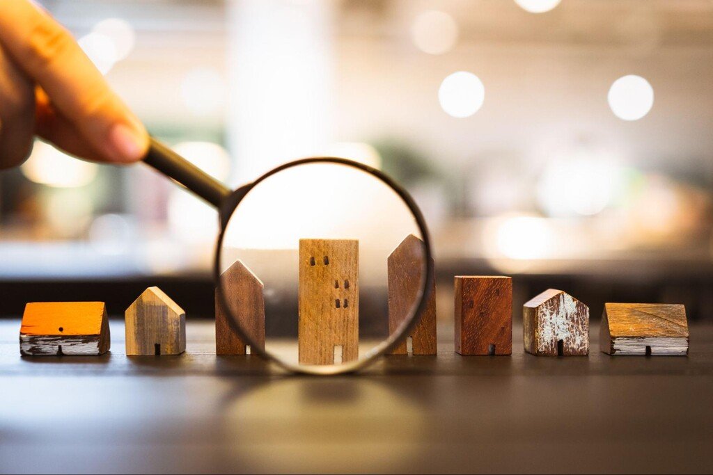 lupa em frente a casas em miniatura, ilustrando o tópico sobre como começar a investir em imóveis