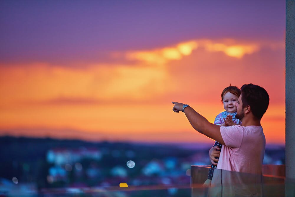Homem segurando um bebê apontando para o céu em uma cobertura