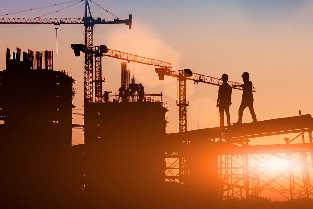Dois homens em cima de uma táboa de construção olhando para outros homens em ambiente de construção