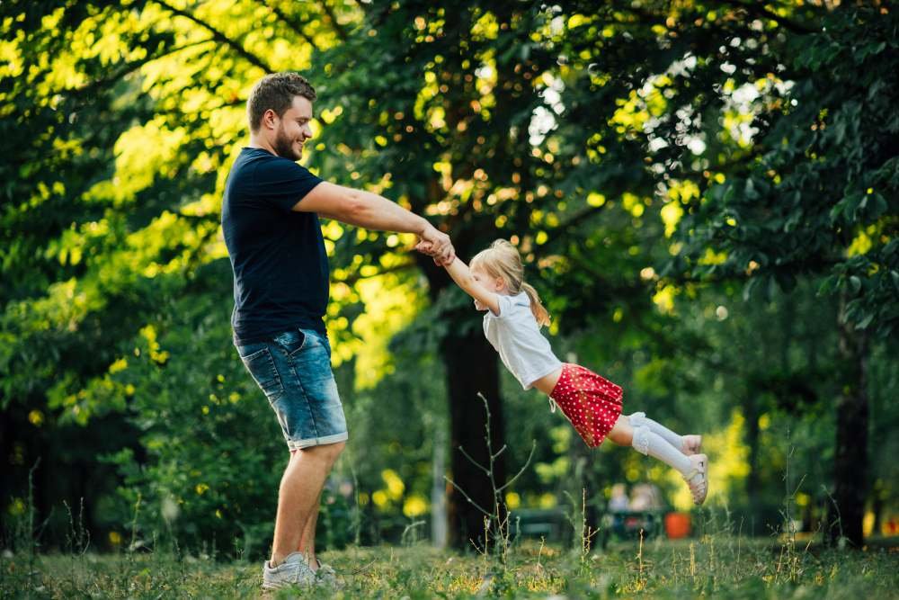 Homem segurando as mãos de menina e se divertindo com árvores atrás em Moema