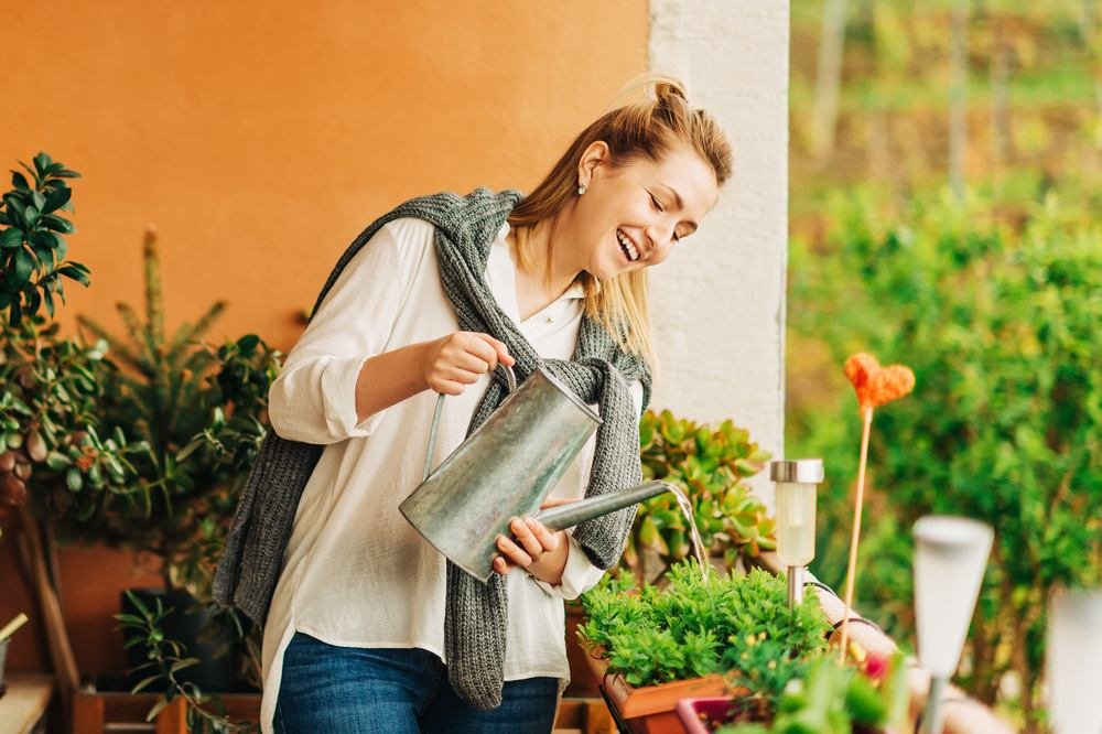 Mulher cuidando de plantas de um jardim, possivelmente de um espaço de um apartamento garden