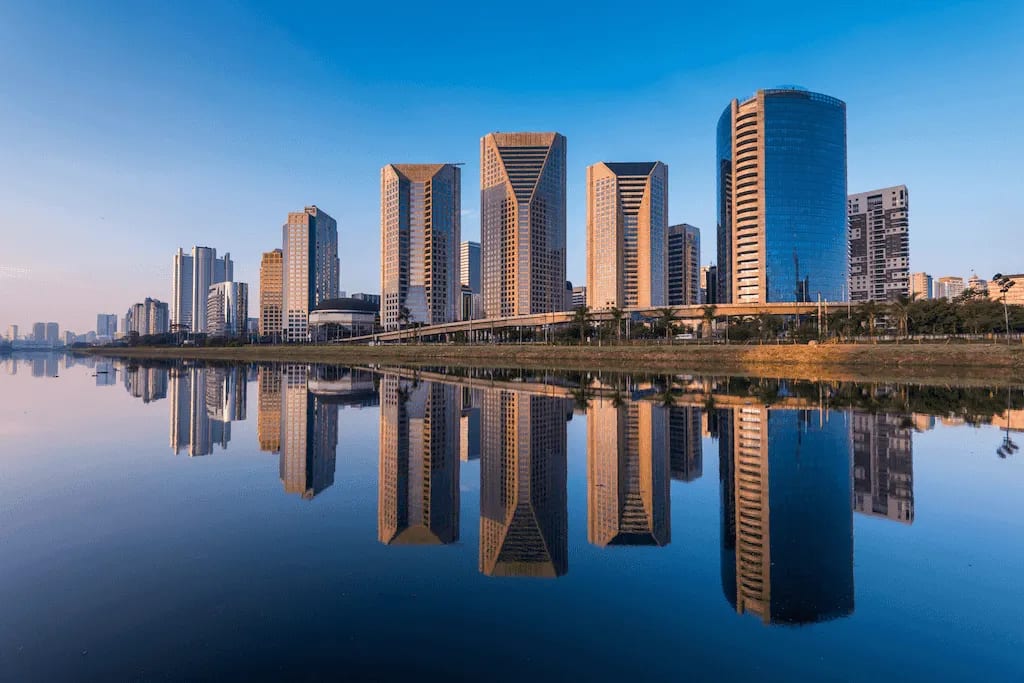 Conjunto de prédios modernos refletidos no rio Pinheiros ao amanhecer, mostrando a arquitetura contemporânea de São Paulo.