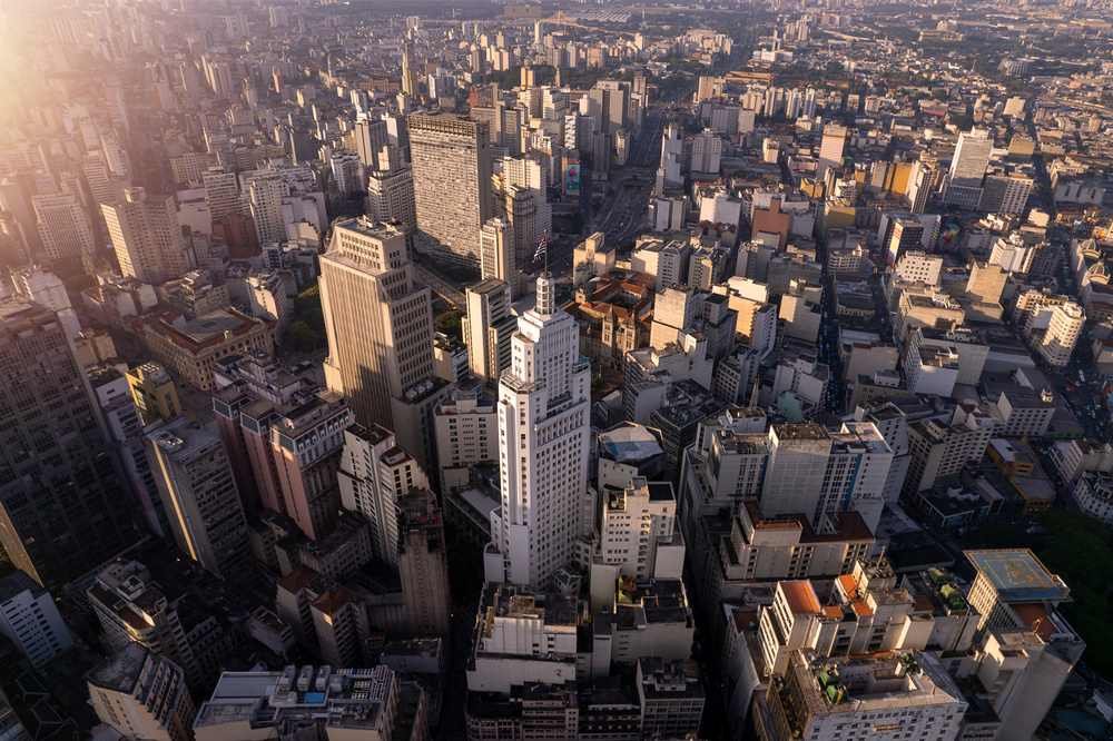 Imagem aérea de São Paulo com prédios altos e cidade vasta ao entardecer.